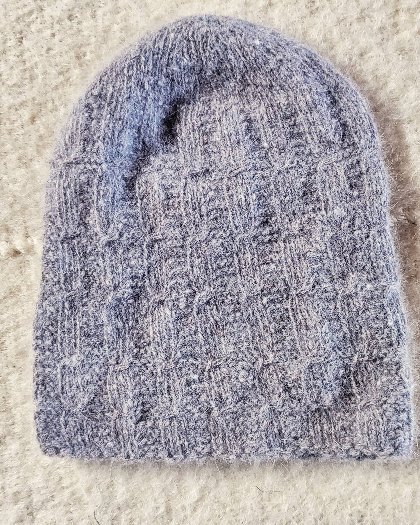 Blue knitted angora wool hat on a beige carpet