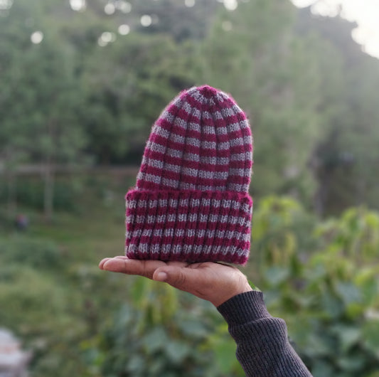 A hand holding a multicolored ribbed beanie hat against a blurred natural background.