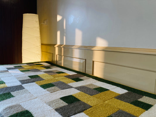 A multicolored geometric patterned throw draped over the edge of a couch, with a lamp and wall in the background.