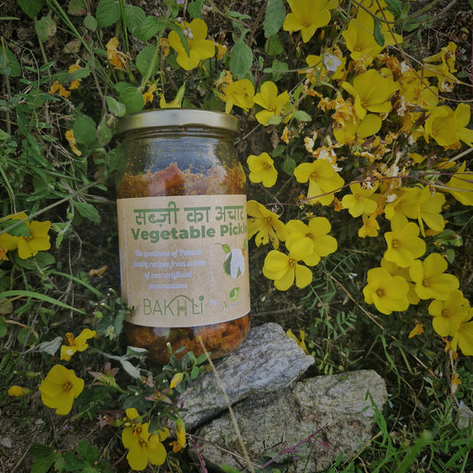 A jar of vegetable pickle placed on a rock surrounded by yellow flowers.