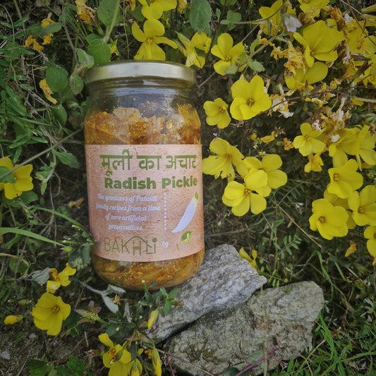 A jar of radish pickle placed on a rock surrounded by yellow flowers.