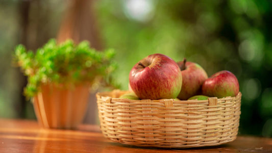 A handcrafted bamboo fruit basket filled with red apples, placed on a table with a blurred background.