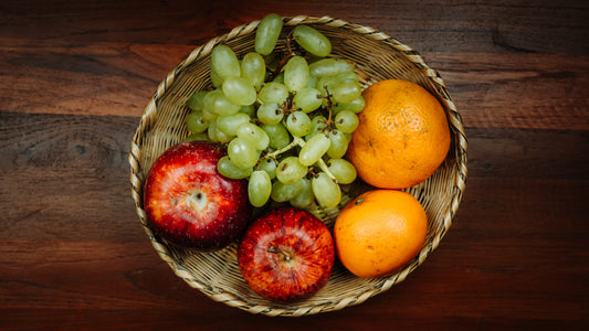 A handcrafted Ringal fruit tray filled with grapes, an orange, and two apples on a wooden surface.