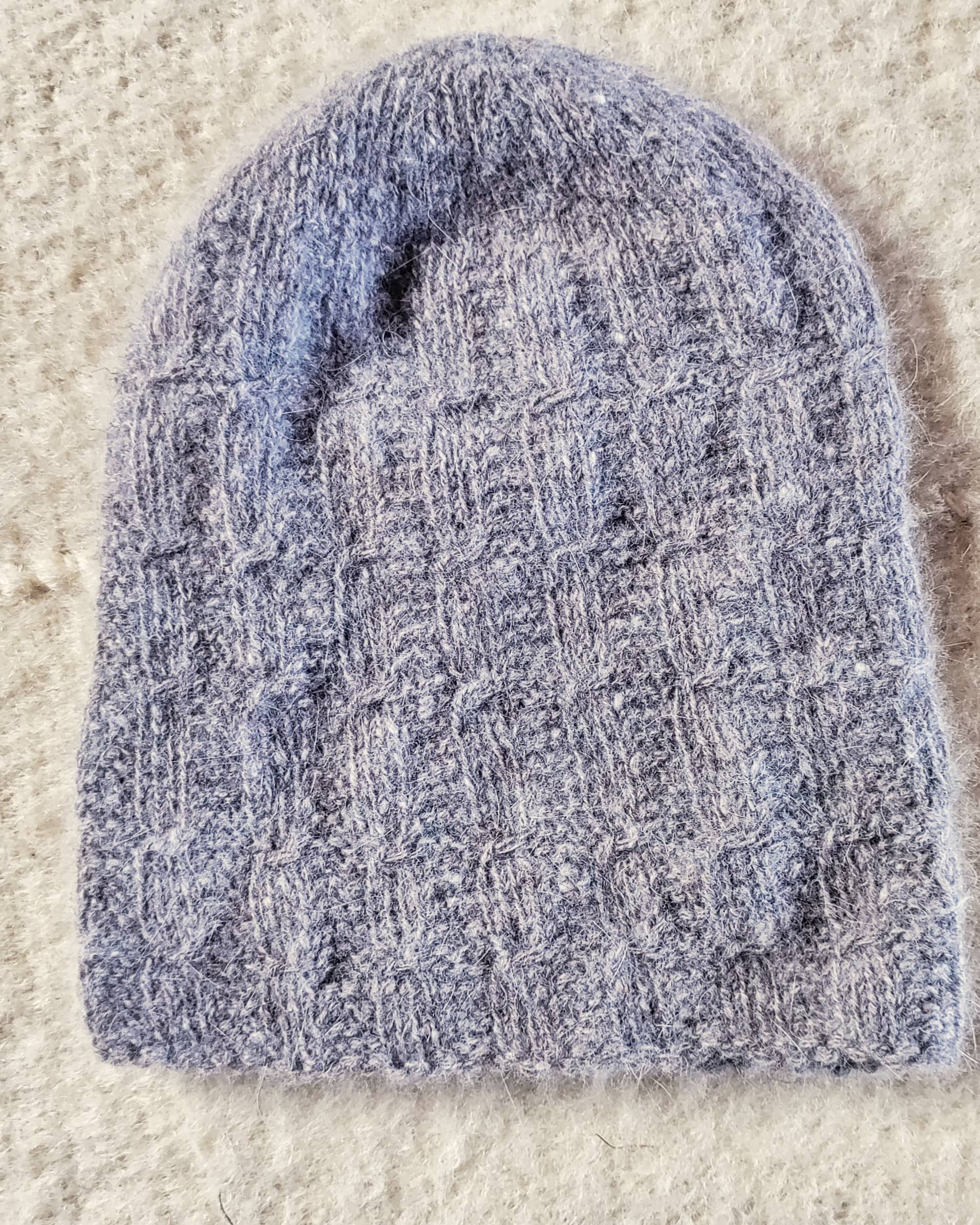 Blue knitted angora wool hat on a beige carpet