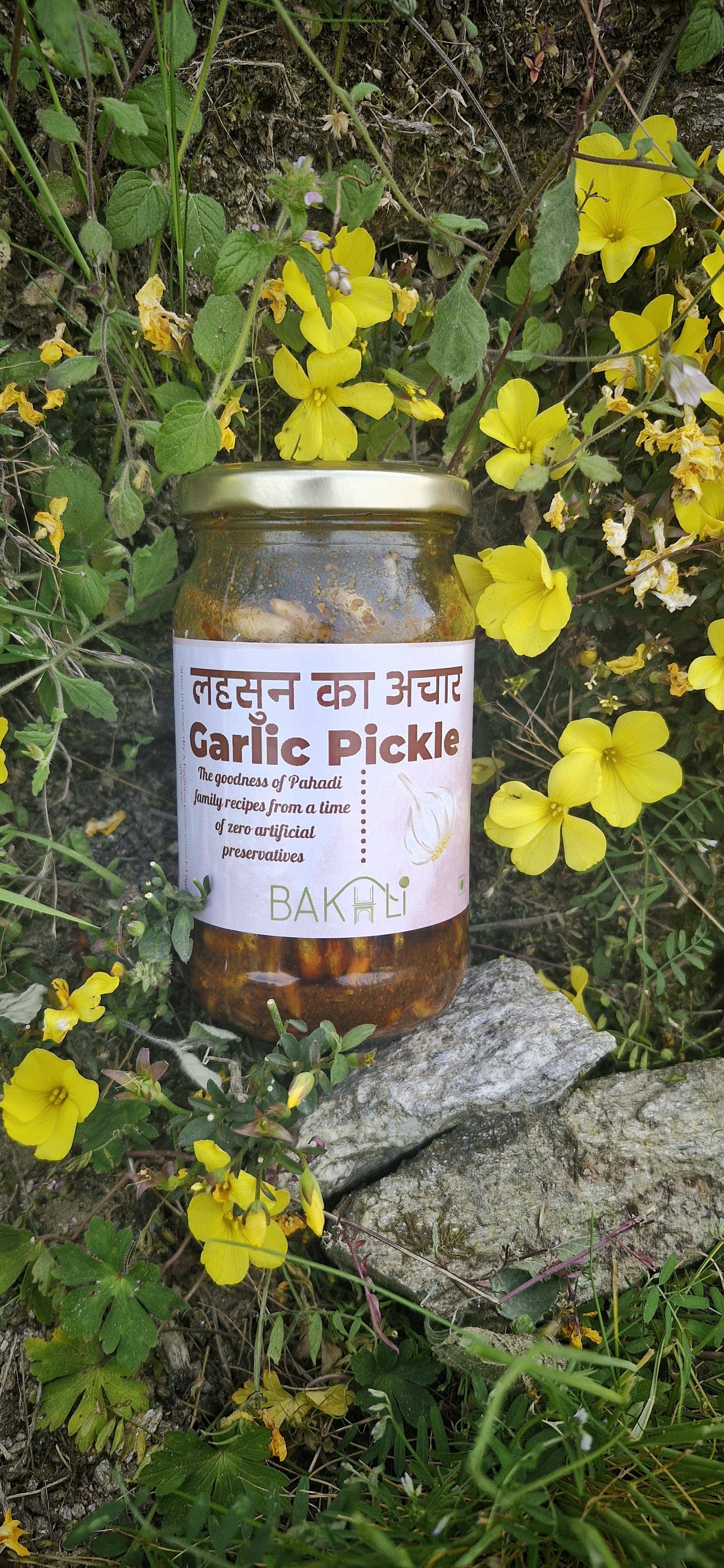 Jar of garlic pickle with a label on a rock surrounded by yellow flowers