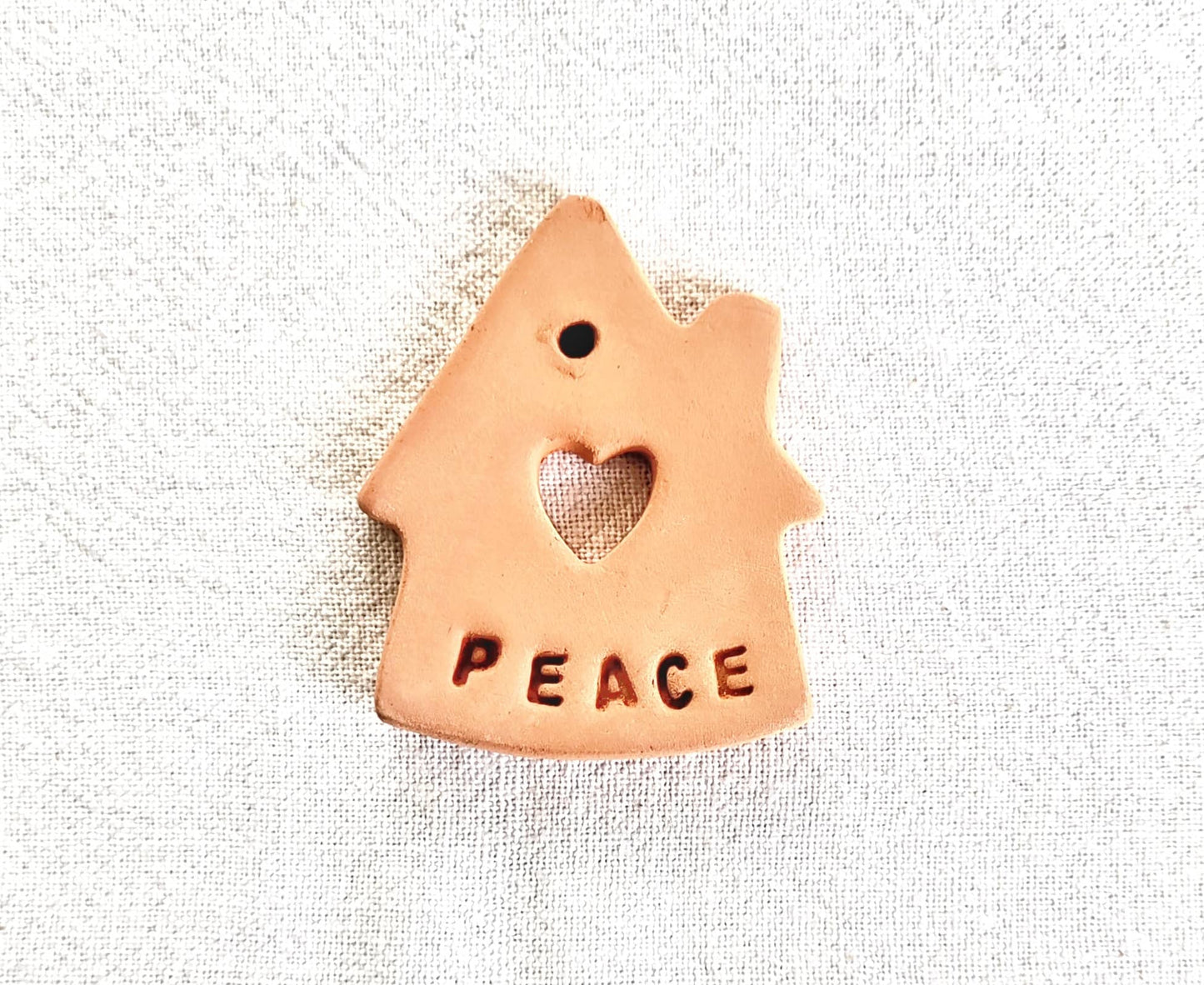 Ceramic house-shaped ornament with 'PEACE' and a heart on a textured white background