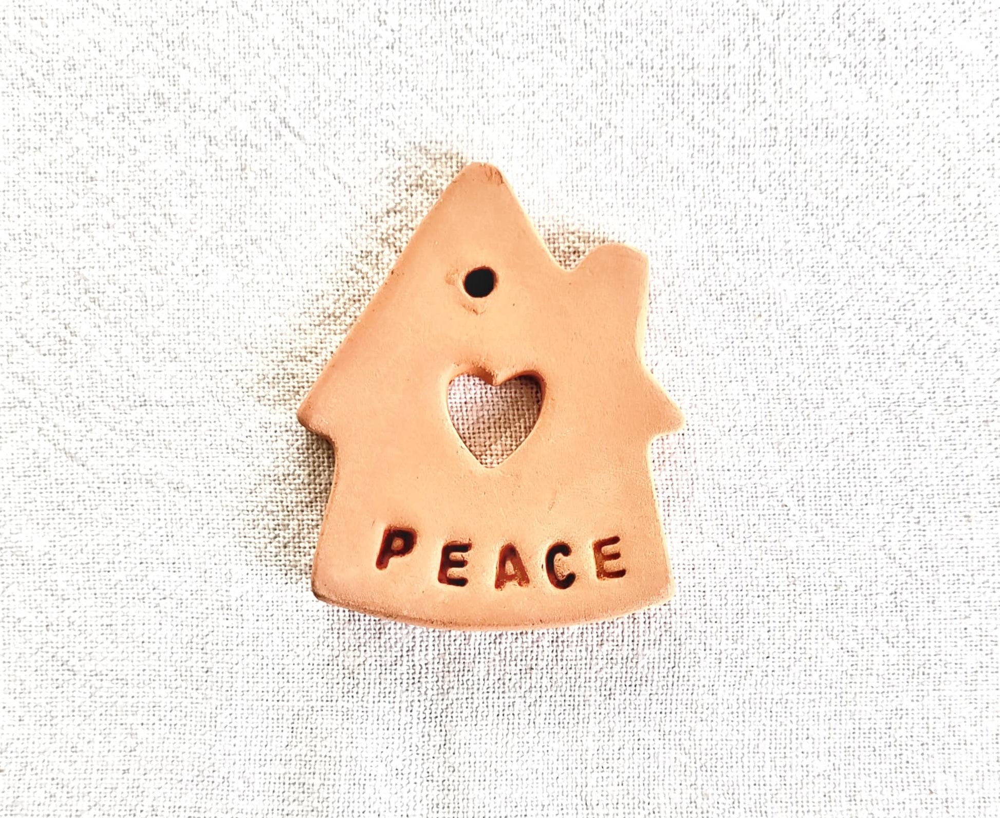Ceramic house-shaped ornament with 'PEACE' and a heart on a textured white background